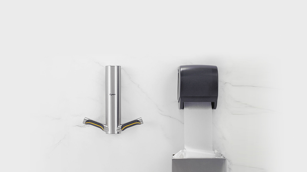 Un secador de manos Dyson Airblade 9kJ montado junto a un dispensador de toallas de papel.